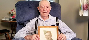 image of Gilbert sitting on a sofa while holding a photo of himself in uniform.