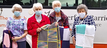 Four female members of the knitting group at Waterford Barrie Retirement Residence, showcase four of the afghans they generously donated and delivered to Hospice Simcoe.