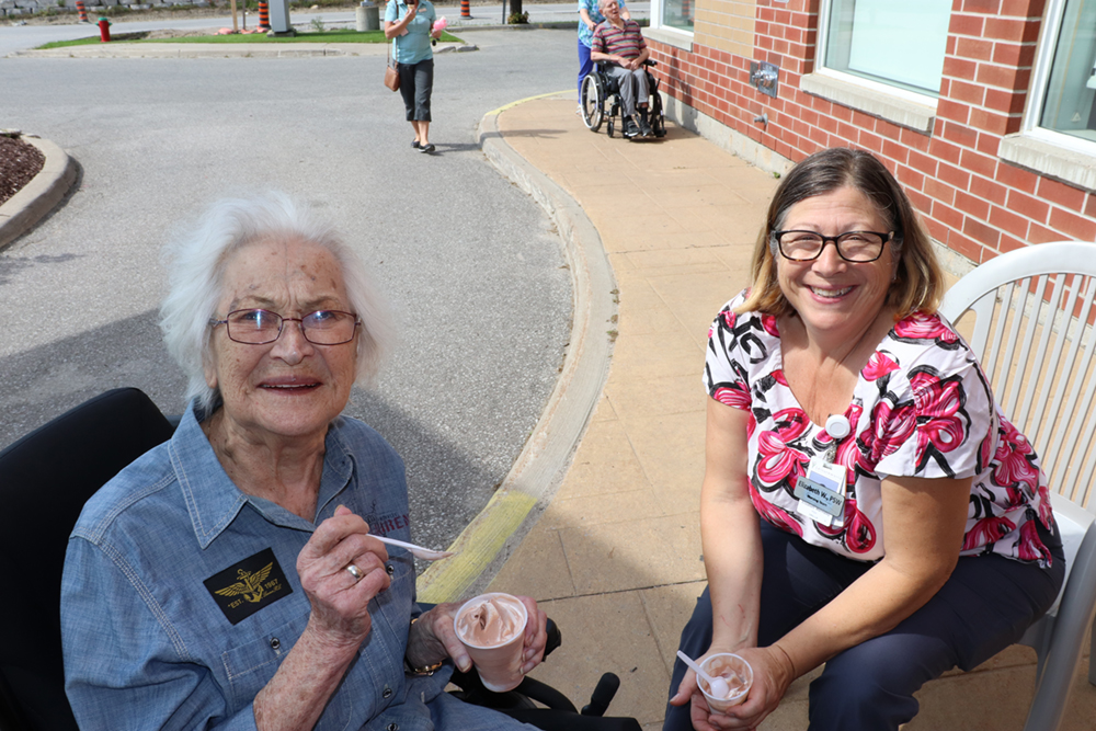 A team member and resident sitting together eating ice cream.  