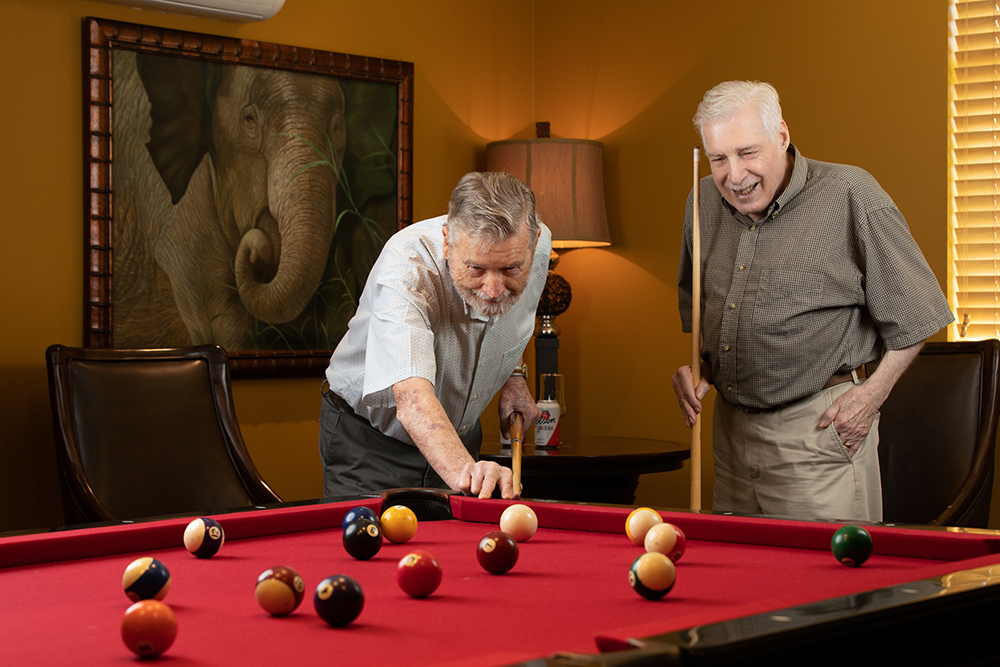Two men laughing while playing billiards in a living room