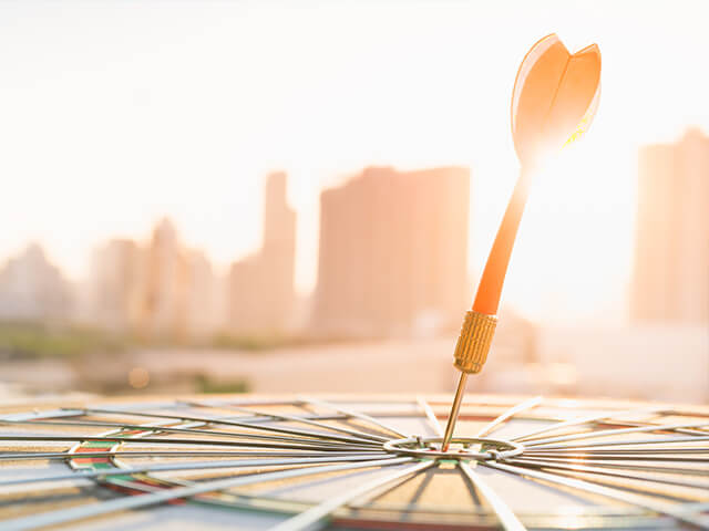 image of a red dart arrow hitting in the target center of dartboard with modern city and sunset background.