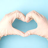 close up photo of hands in gloves making giving shape of heart with fingers isolated over blue background
