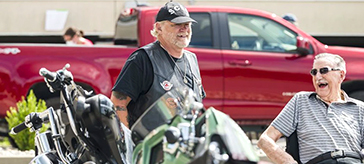  Two older motorcyclists smile in front of their motorcycles