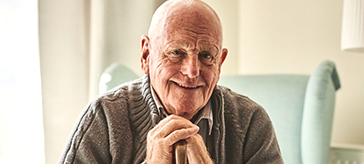 Portrait of happy senior man sitting at home with walking stock and smiling