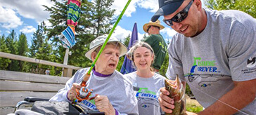 image of Nathan Ondrus (right) shows Jane MacKay, a resident of Mariposa Gardens, the large rainbow trout she’s just reeled in.