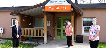 Team members from Muskoka Shores Care Community stand by the entrance of the care community at a safe distance