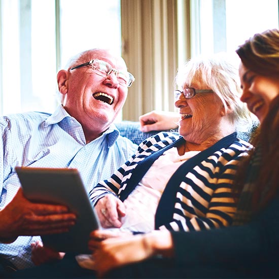 image of a cheerful senior man with his wife and daughter siting on a couch and laughing together