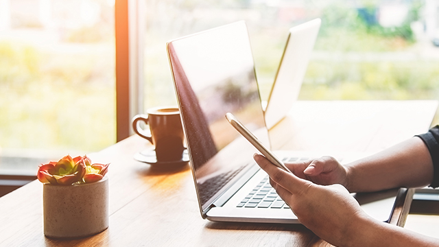 Young woman sitting at cafe table drinking coffee and working on laptop.