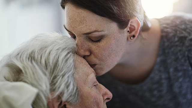Woman kisses elderly mother's forehead