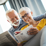 Closeup low angle view of a mid 60's couple sitting on a couch and reading magazines. They are talking and sharing some laughs.