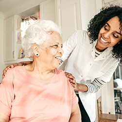 image of a young lady assisting a female senior and they both smile towards each other.