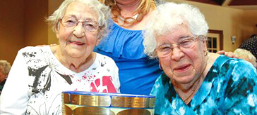 image of 2 residents from Waterford Kingston and one of the team members smiling toward the camera while holding a very big coffee cup